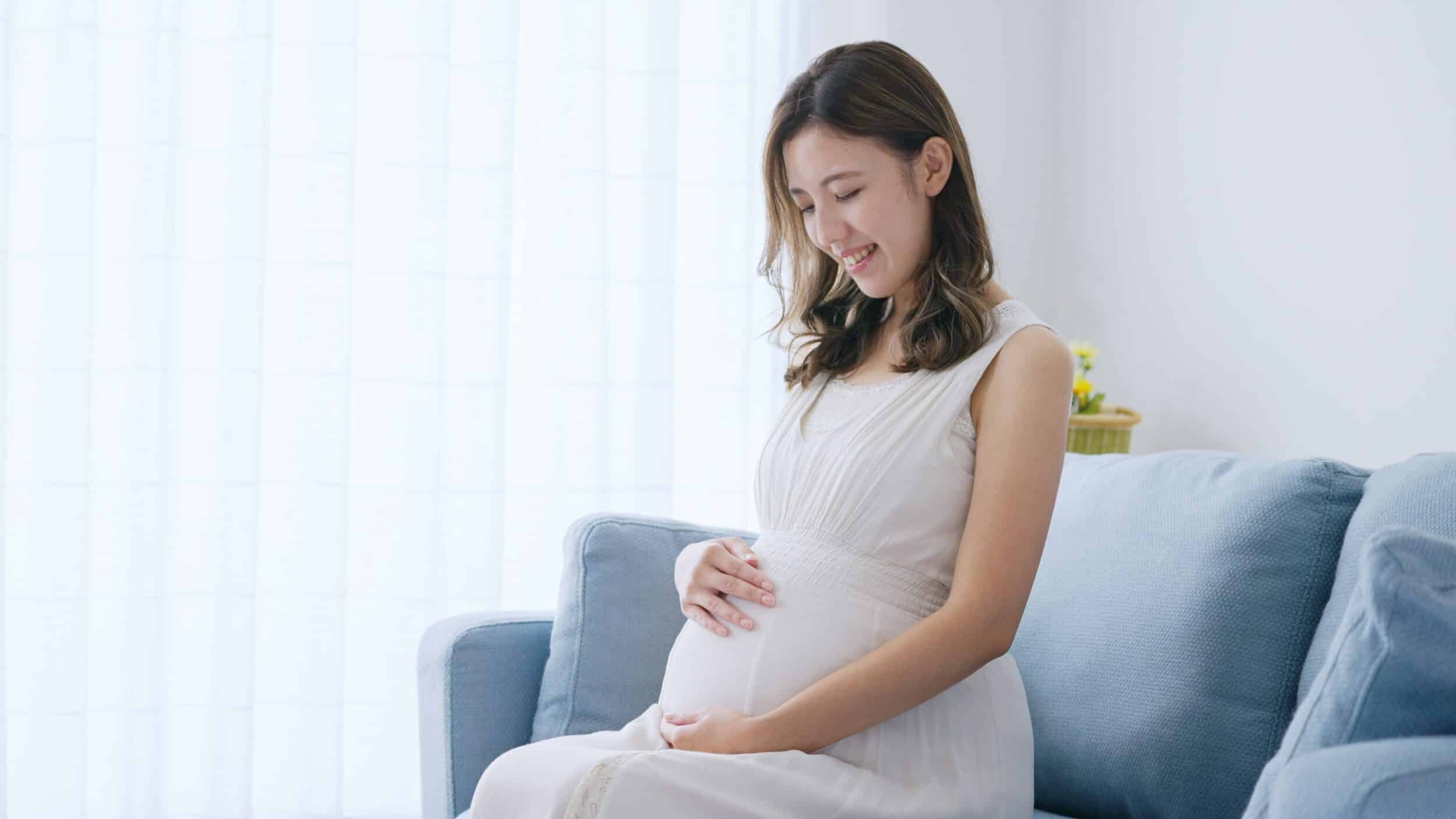 A pregnant woman sitting on a couch holding her belly